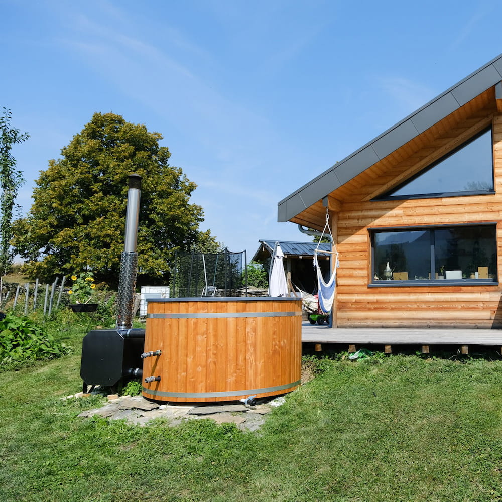 Bain nordique en bois installé dans le jardin à proximité d'une maison et de sa terrasse
