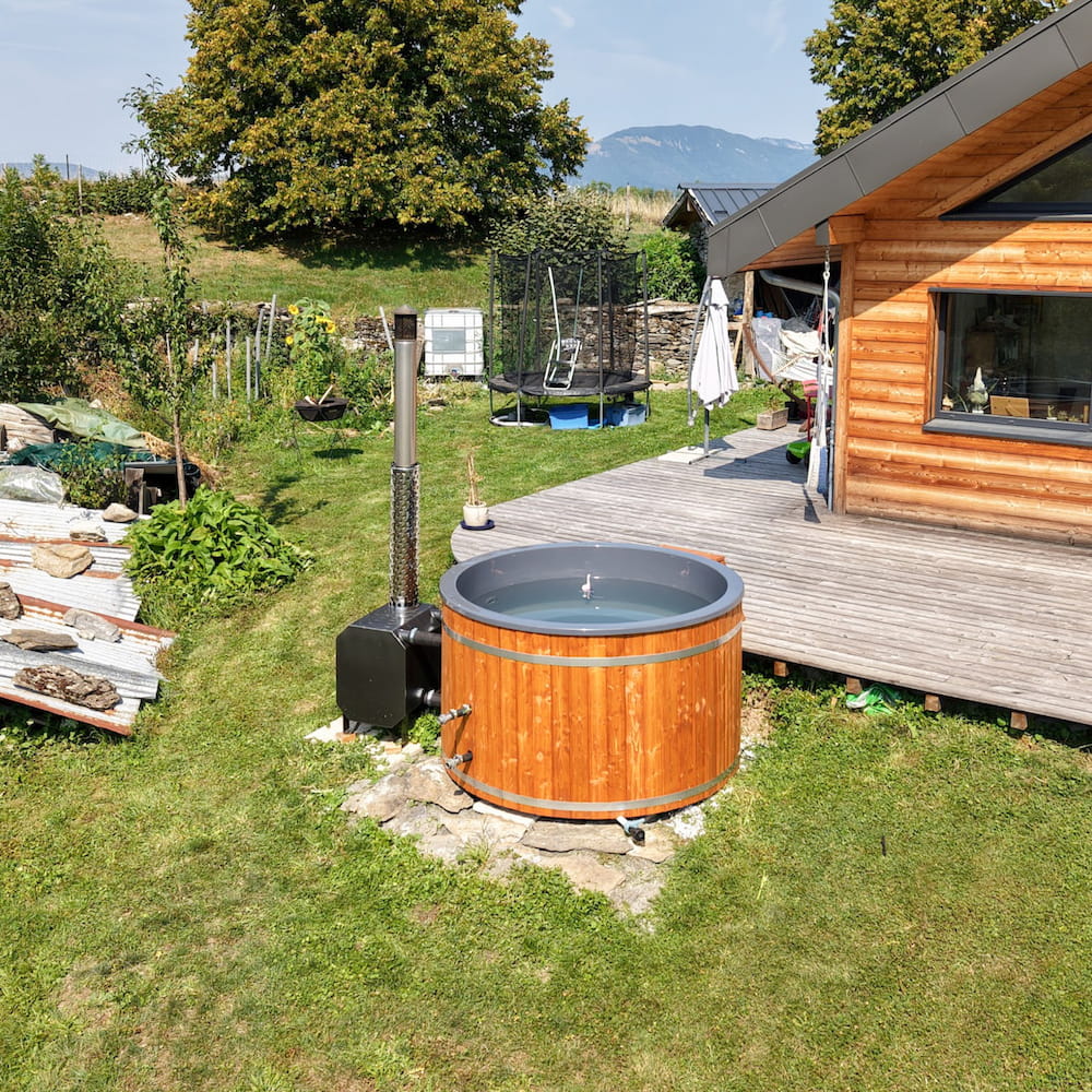 Bain nordique en bois installé dans le jardin à proximité d'une maison et de sa terrasse