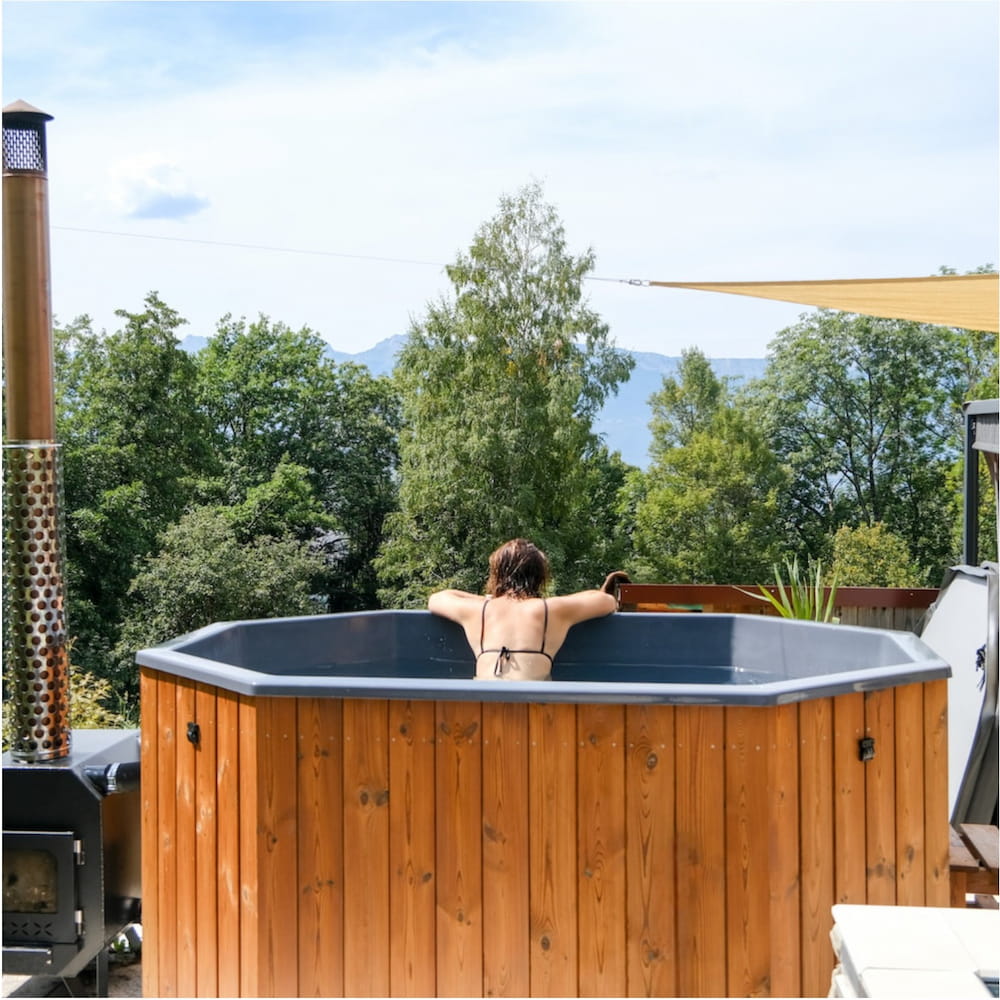 Personne dans un bain nordique octogonal en bois avec cheminée et terrasse extérieure